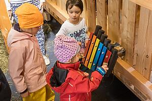 Kinder spielen auf einem Xylophon an der Wand im Heuschober des Spielplatzes